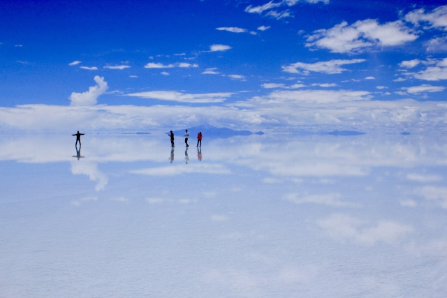 雨季のウユニ塩湖で空と雲が湖面に映り込み、人物が小さく写る風景