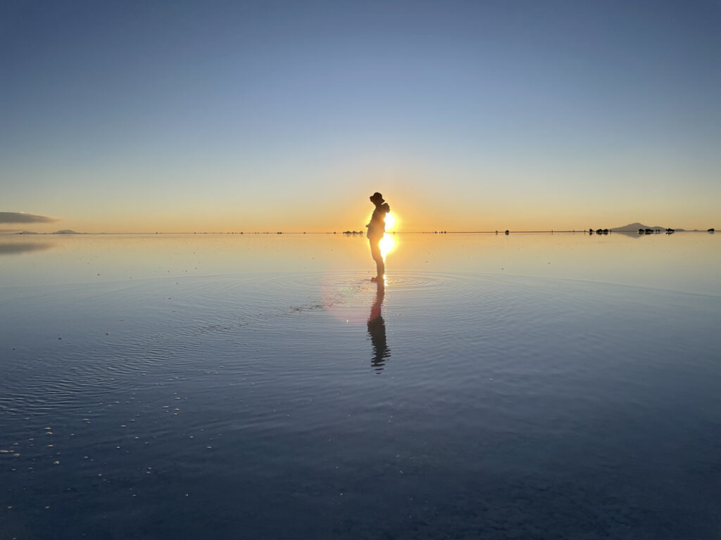 ウユニ塩湖の夕日と鏡張りに映る人物のシルエット。絶景とリチウム資源の現実が交錯する場所
