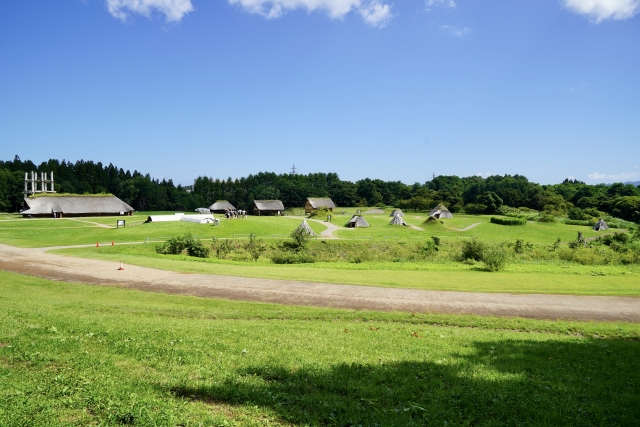 青森県の世界遺産・三内丸山遺跡に復元された竪穴住居と緑の森が広がる風景。縄文人が森を育てながら暮らした集落跡