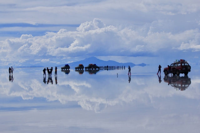 ウユニ塩湖の水面に人や車、雲が上下対称に反射して映る鏡張りの風景