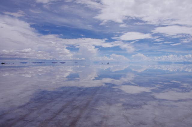 浅い水の下に白い塩の地表が見え、空と雲が同時に反射しているウユニ塩湖の風景