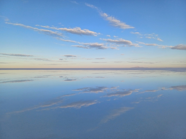 ユニ塩湖の平らな水面に空と雲が歪まずに反射し、一直線の地平線が見える様子