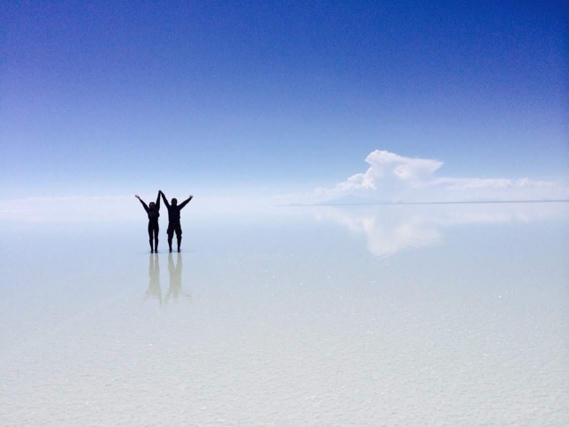 ユニ塩湖の水面に空と雲が反射し、水平な地平線と人物が映り込む鏡張りの風景