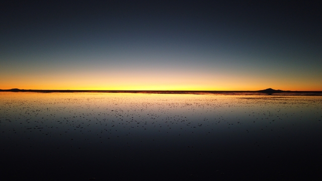 夕暮れのウユニ塩湖で、空と水面の境界がほとんど見えなくなった鏡面の風景
