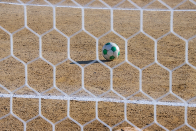 六角形の網目をしたサッカーゴールネット越しに見えるサッカーボール