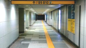 地下駅の長い通路に出口案内板が並ぶ、迷いやすさを感じさせる地下通路の風景