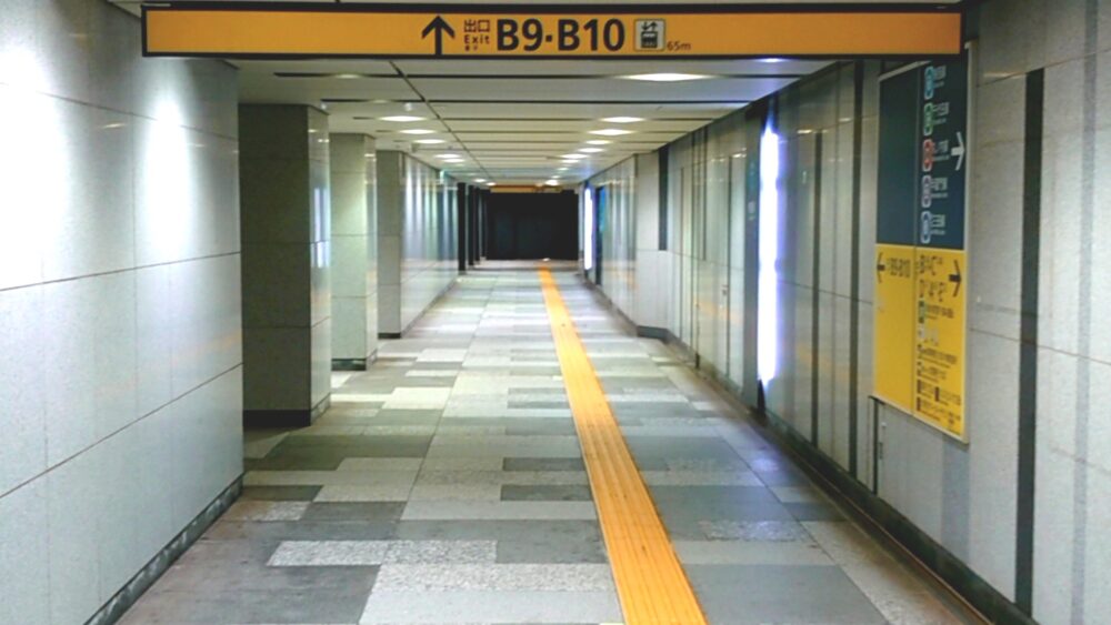 地下駅の長い通路に出口案内板が並ぶ、迷いやすさを感じさせる地下通路の風景