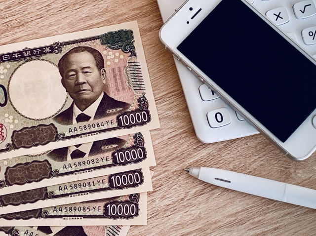 一万円札とスマートフォン、電卓が並ぶお金の記録を表すイメージ